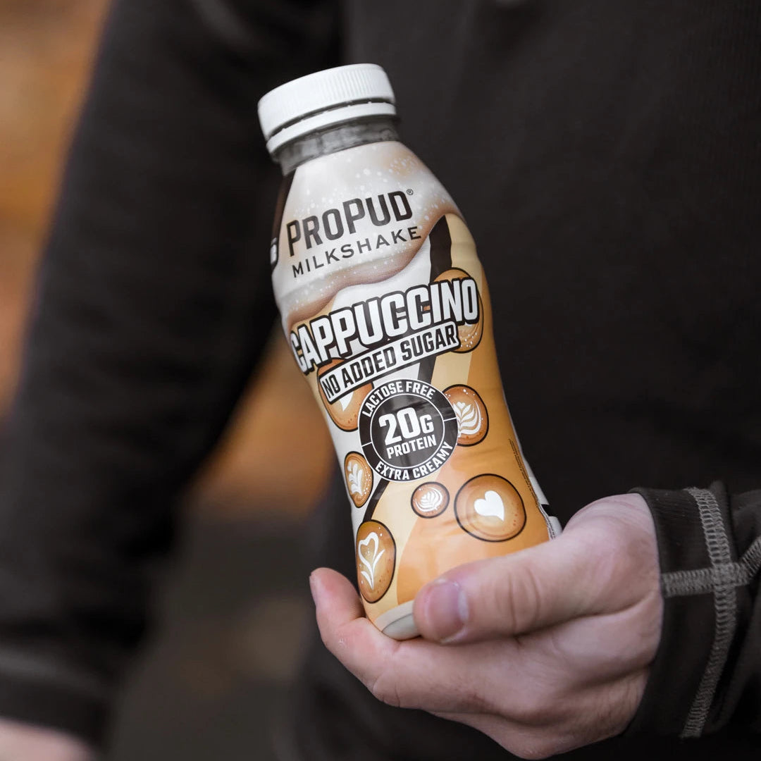 A person in a black hoodie holds a bottle of Propud Milkshake Cappuccino with Moder Sugar, 20g sugar, 3.5 cups milkshake.