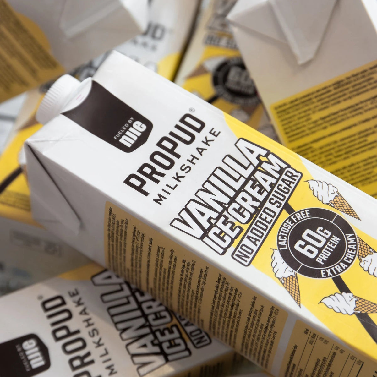 A close-up pile of Propud Milkshake vanilla ice cream carton packaging, showing white and yellow cartons with black branding and product text.